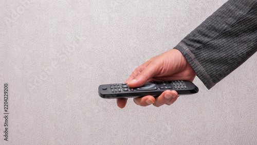 Hand holding a black television remote control. This image is perfect for technology, entertainment, home leisure, and lifestyle media projects.
