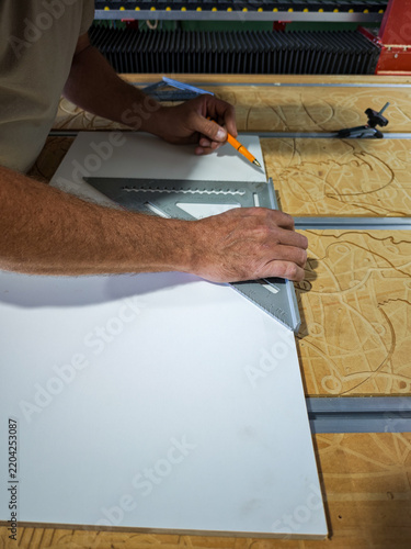 Woodworker measuring white panel with speed square and pencil on CNC machine bed