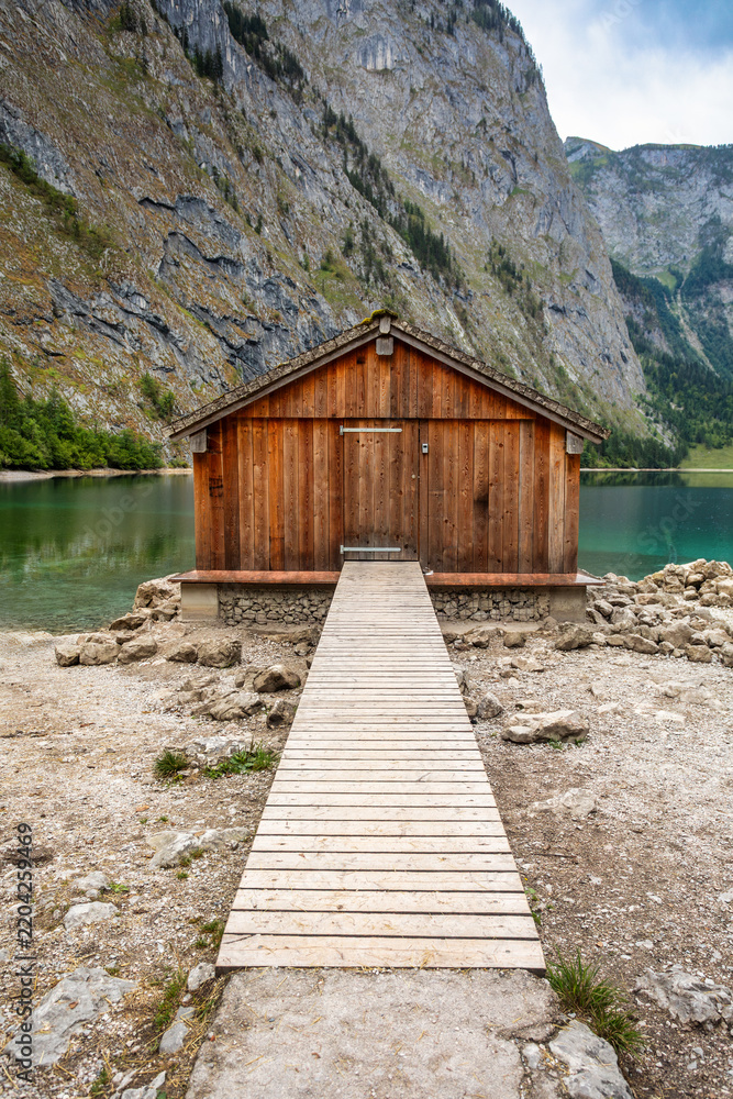 Fototapeta premium Wooden boathouse with walkway on shore of clear green mountain lake Germany