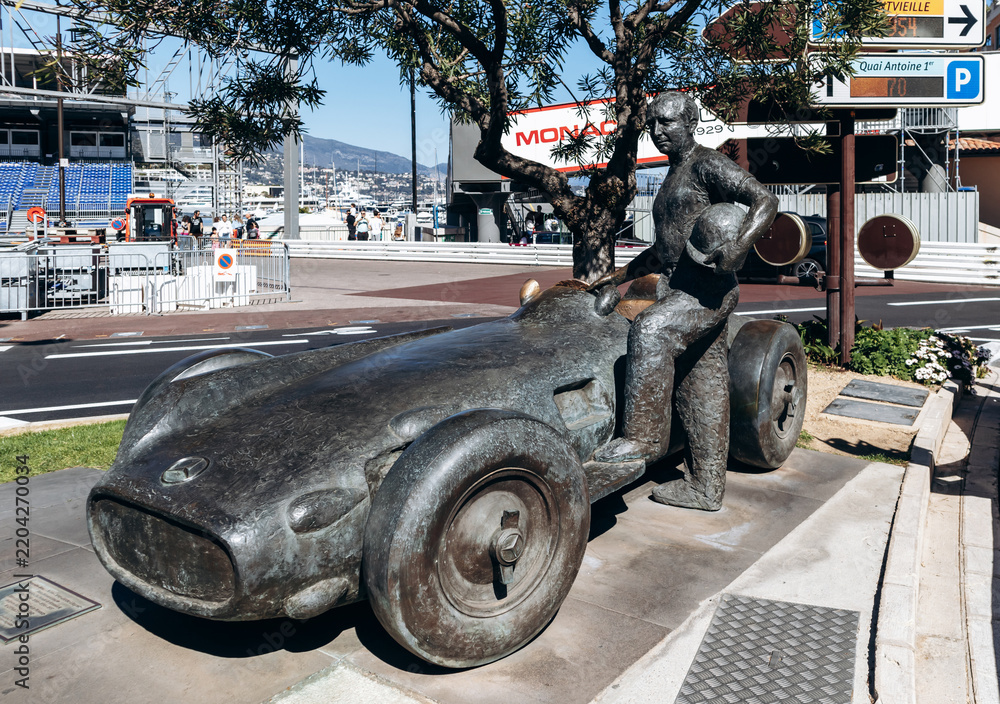 Obraz premium Monaco, Monaco - April 04, 2026: Bronze monument to Juan Manuel Fangio beside a Mercedes-Benz W196 race car near Port Hercule in La Condamine.