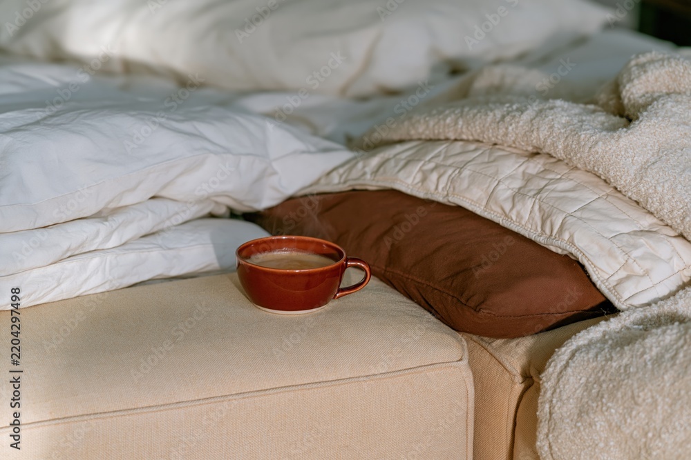 Obraz premium Coffee cup steaming on a yellow sofa arm beside plush cushions and a throw blanket, a cozy home scene for relaxation and autumn breaks
