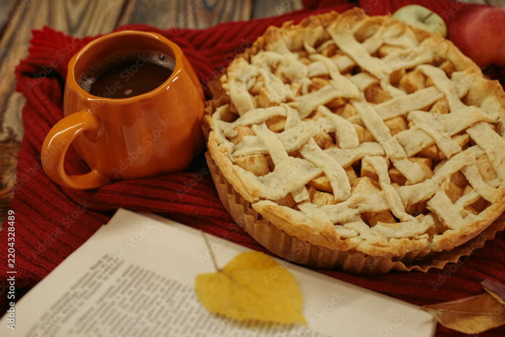 Naklejka premium Homemade apple pie with a lattice top next to a cup of hot coffee and an open book, autumn leaf decor, cozy autumn reading setting, film grain effect, high-quality photo