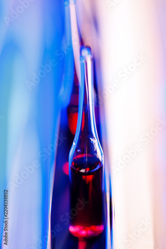 Vertical close-up of single glass ampoule with red solution for pharmaceutical laboratory background and medical research