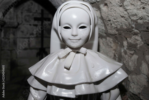 Creepy white nun doll with black eyes standing in an ancient stone building