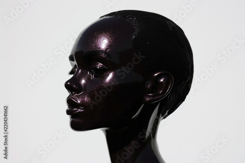 Conceptual artistic portrait of a woman with metallic dark shimmering skin in profile