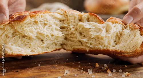 Hands tearing apart a golden brioche loaf, revealing a soft fluffy interior and shiny crust with coarse salt on a rustic wooden board
