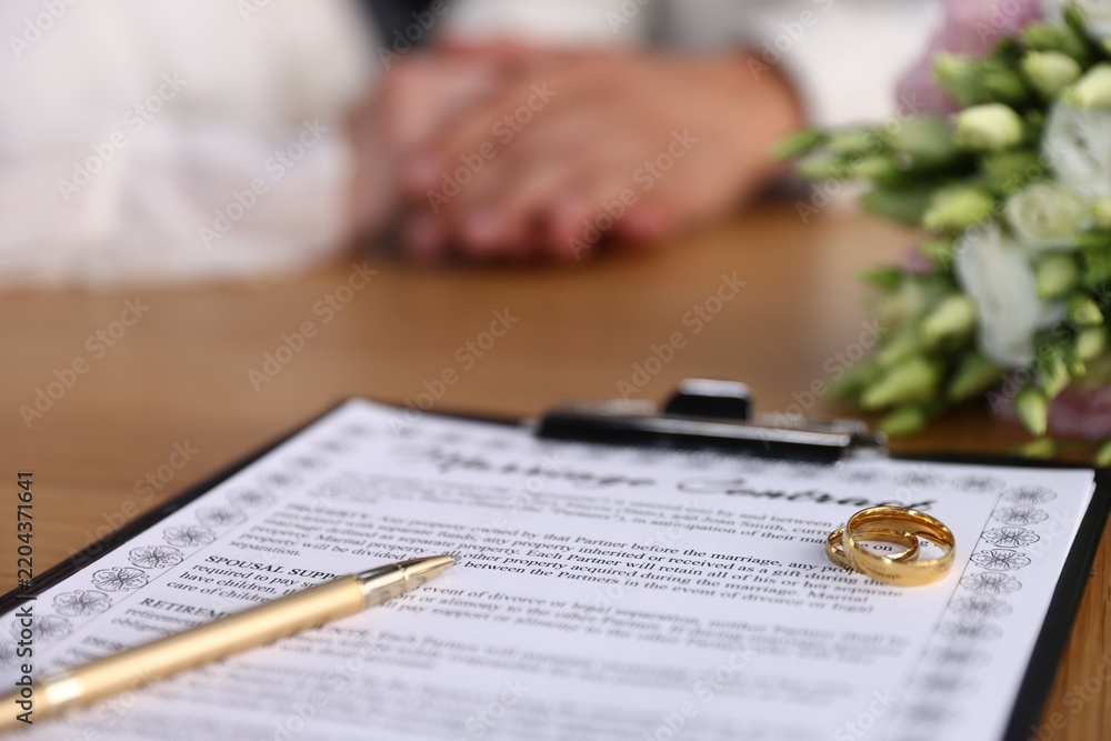 Obraz premium Marriage contract, wedding rings and couple at wooden table, selective focus