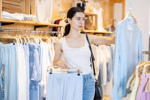 Фотография Girl in clothing store chooses several items of clothing, makes up summer look