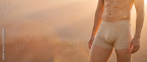 Man in beige boxer briefs standing outdoors in warm golden sunlight with copy space