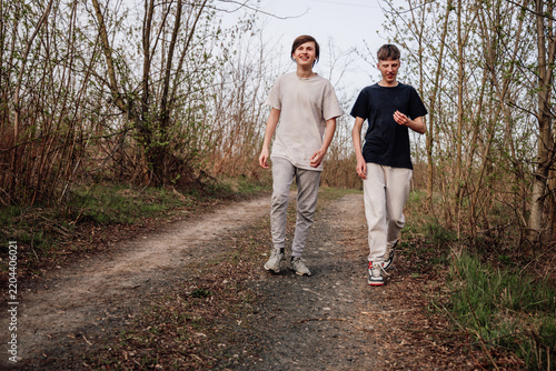 Two boys walk on a dirt path in a forest area