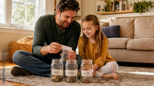 Father and daughter saving money in glass jars, financial education for children at home, happy family teaching investment and budget habits