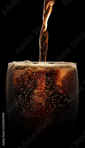 Dark fizzy drink pouring into a glass on black