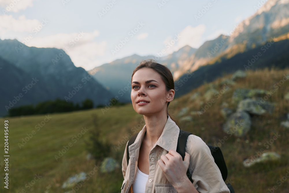 Obraz premium Woman traveler hikes through a sunny meadow with a backpack, enjoying nature and dramatic mountains, a candid outdoor lifestyle moment amid expansive scenery and peaceful solitude outside.