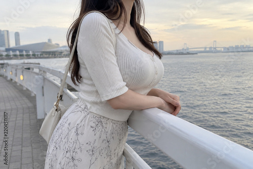 Obraz w ramie 水辺の白い手すりに腕を置く白いリブニットと花柄スカートの女性