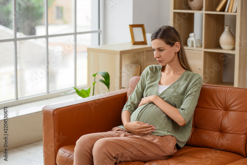 Pregnancy anxiety and prenatal stress, worried pregnant woman sitting on sofa...