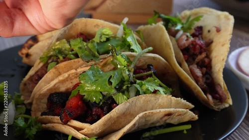 Adding salsa to tacos filled with grilled chorizo, cilantro, and onion, resting on a dark plate. Ideal for food blogs.