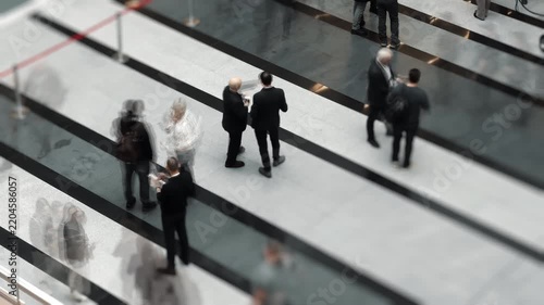 Two people stand and talk while a blurred crowd moves rapidly around them in time lapse. Concept of busy life, human connection, communication and fast-paced society.V