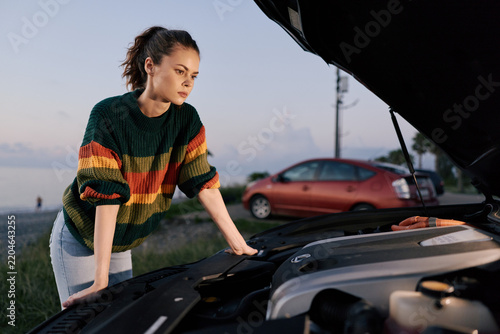 Foto Woman looking under the open hood of a broken car on the roadside