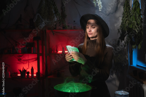 Fotografie Realistic witch brewing a potion in cauldron counting money dollars from her small business