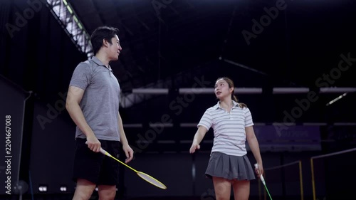 Asian male coach guiding young girl through badminton swing technique on indoor court