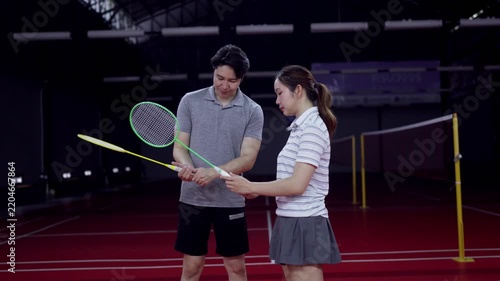 Asian male coach teaching young woman proper badminton racket grip on indoor court