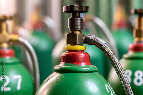 Close-up of green oxygen cylinders with high-pressure valves and braided hoses, industrial gas storage system in factory or medical facility.