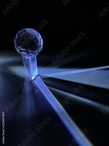 Faceted crystal sphere on transparent stand surrounded by dramatic blue light rays on dark background.