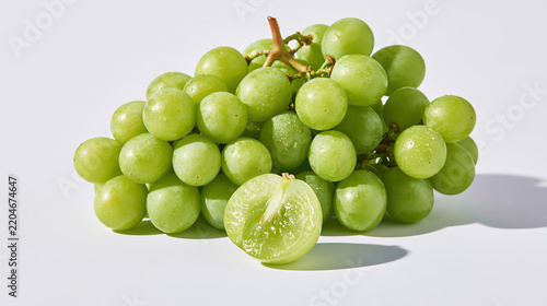 Fresh green grape cluster with plump fruit and sliced grape on pale surface, creating crisp natural food still life with soft shadow