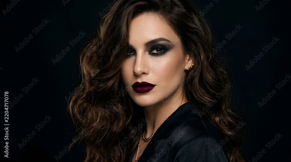 Fototapeta premium A stunning young woman with dramatic makeup and wavy dark hair poses for a fashion beauty portrait in studio lighting