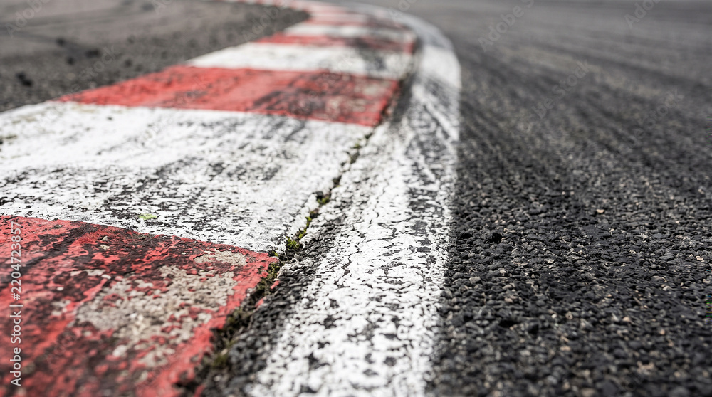 Obraz premium Textured Asphalt Race Track Surface with Red and White Apex Curb and Rubber Skid Marks, Low Angle Perspective of Motorsport Circuit for Speed and Automotive Design Concepts