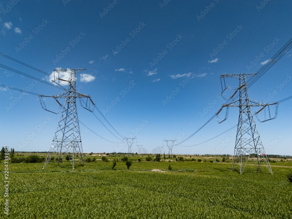 Obraz premium Transmission towers standing in green fields under blue sky
