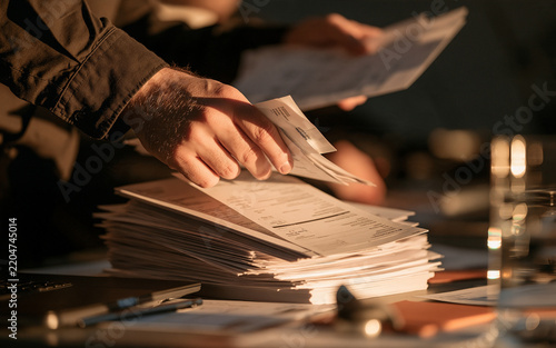Close up of hands sorting through business documents and reports on a desk, paperwork and office organization concept, warm office lighting