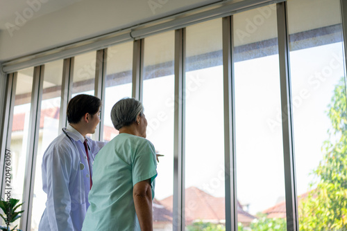 Doctor talking with senior woman by bright window from behind