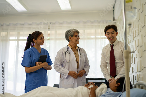 Hospital doctor and nurse smiling with visitor at patient bedside