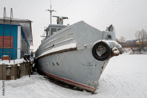 Snow-Covered Boat Moored Beside Dock In Winter Harbor Near Frozen Shoreline
