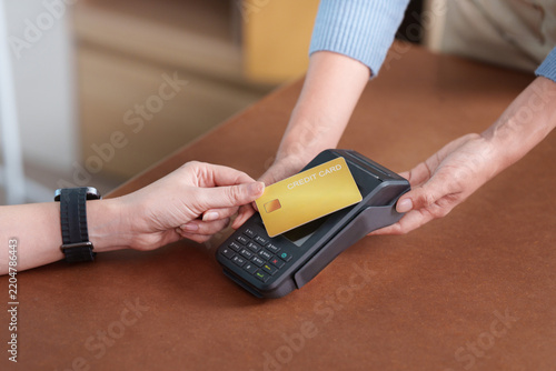 Customer paying with contactless credit card on POS terminal in small business store