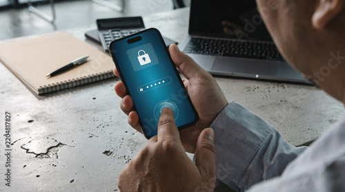 A man securely unlocking his phone with a fingerprint scanner beside a laptop on a wooden desk.