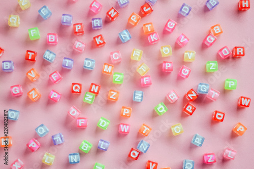 Colorful letter alphabet bead cubes scattered randomly on pink background 