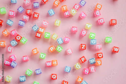 Colorful letter alphabet bead cubes scattered randomly on pink background 