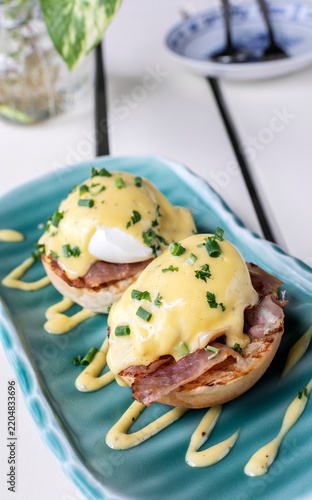Eggs Benedict breakfast food on white table at modern restaurant cafe outdoors