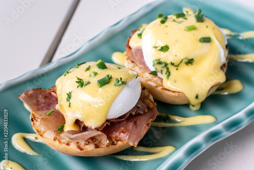 Eggs Benedict breakfast food on white table at modern restaurant cafe outdoors