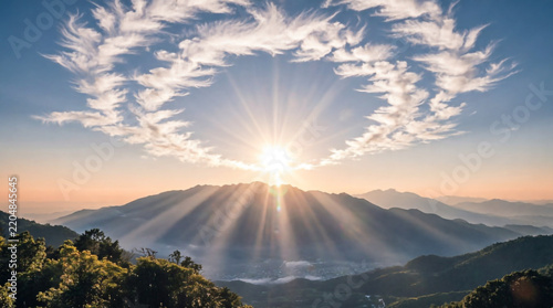 Radiant sunburst rays shine through wispy clouds over mountain peaks at golden sunrise.