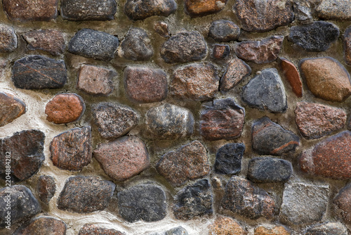 Background of a historic cobblestone wall made of natural fieldstones fixed with cement mortar. Perfect for use as a vintage architectural texture, industrial backdrop, or abstract background