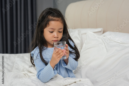 sick preschoool child girl drinking water from glass in bed
