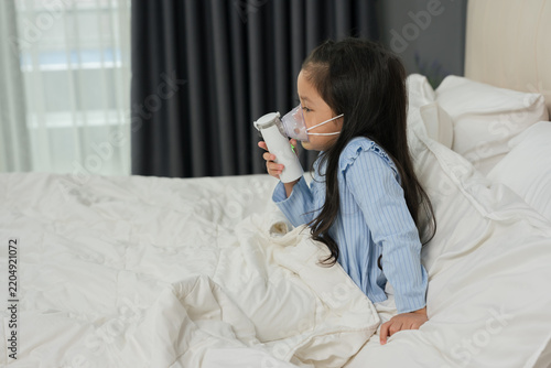 sick preschool child girl using respiratory nebulizer mask in bed