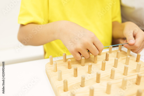 Obraz na plátně Child stretches colored rubber bands around wooden pegs to recreate a geometric pattern on a geoboard during a guided educational activity