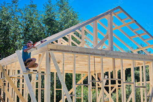 Rafters are secured within timber framework, construction worker uses compact level to ensure precise alignment.