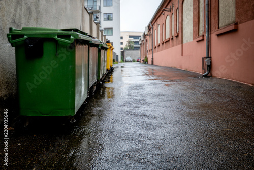 Colorful Waste Bins Along a Rainy Urban Alley