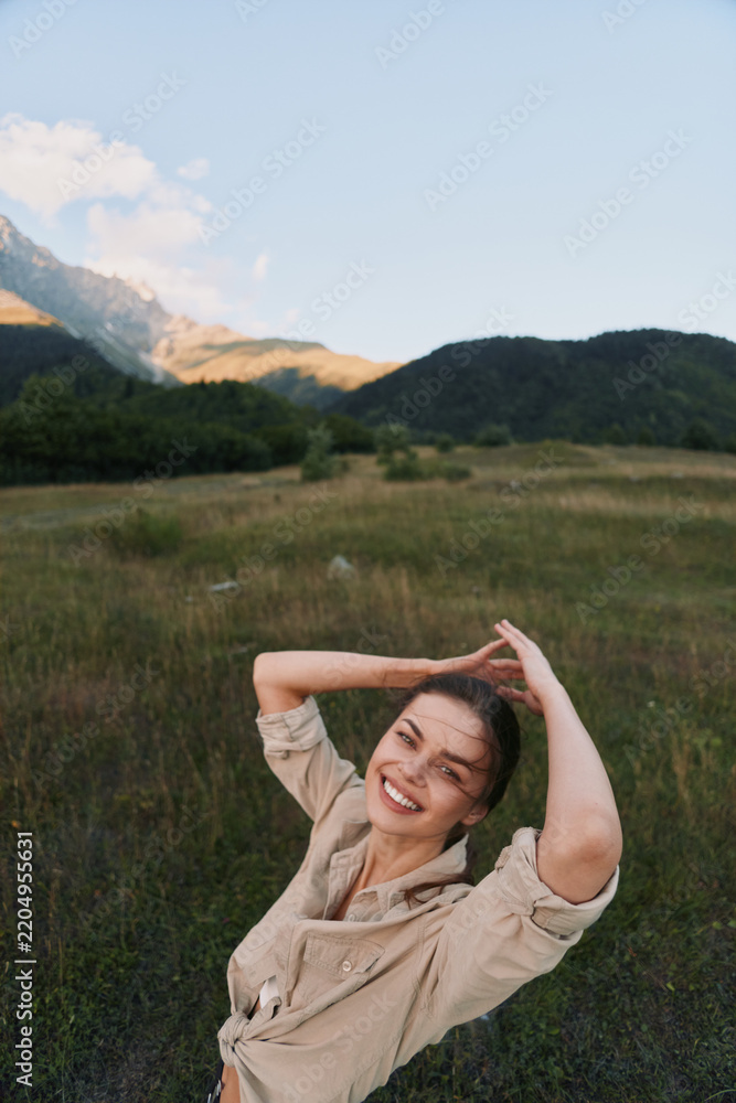 Obraz premium A smiling woman enjoys outdoor lifestyle in a field with distant mountains, capturing a carefree moment in nature in a sunlit meadow, wearing casual attire.