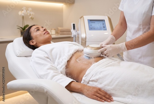 Esthéticienne professionnelle effectuant un traitement de remodelage corporel par cryolipolyse avec de la vapeur froide sur l'abdomen d'une cliente dans une clinique esthétique